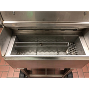 A stainless steel commercial smoker or grill with its lid open, showing the interior chamber, wire racks, and wheels on a tiled floor.