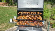 Stainless steel barbecue wheels support a smoker filled with grilled chicken on a sunny day.