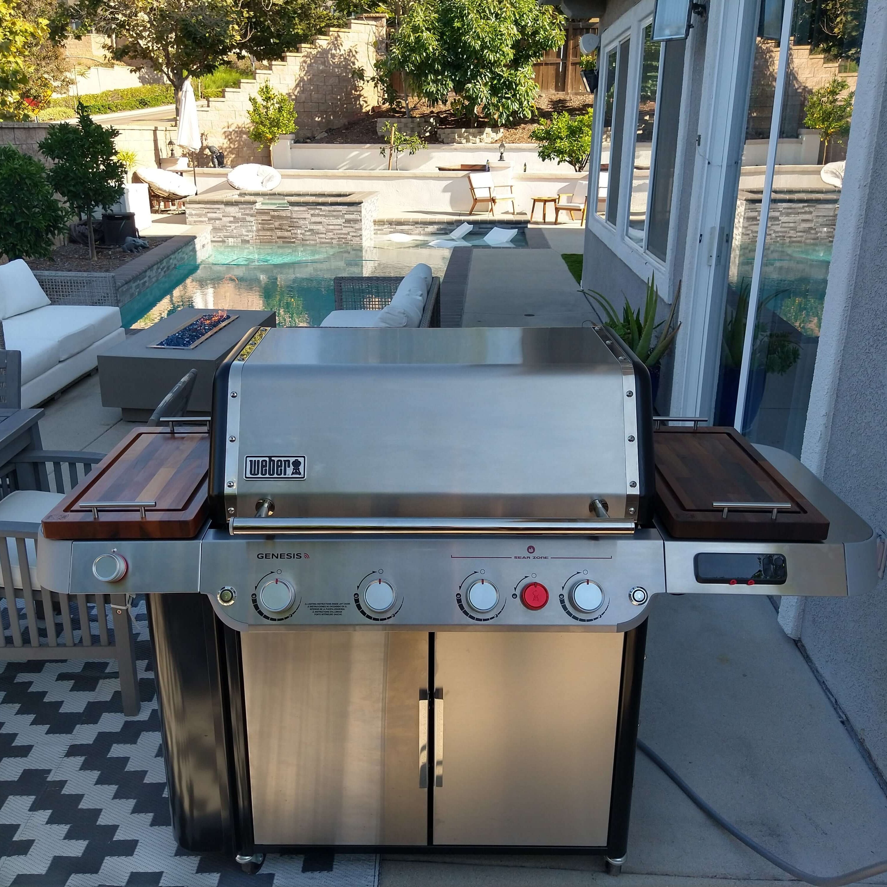Stainless steel barbecue grill on a patio with outdoor furniture and pool in the background