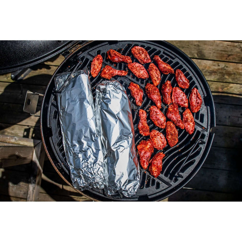 Grilled chicken wings and foil-wrapped dishes on Napoleon charcoal kettle grill cooking surface.