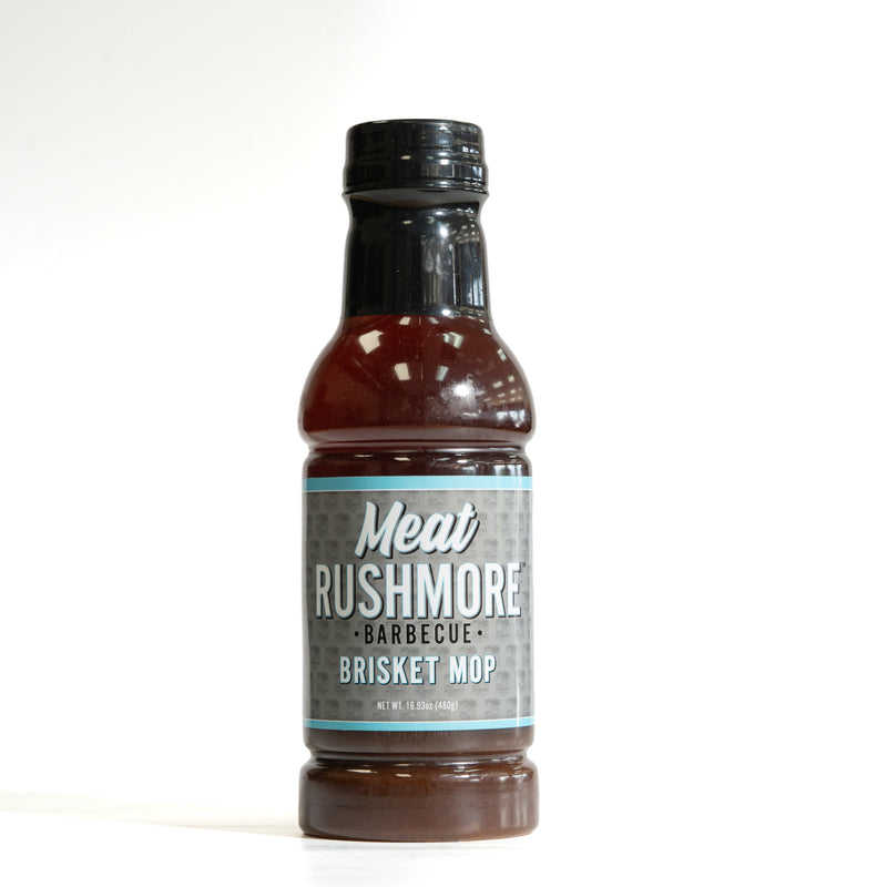 A bottle of Meat Rushmore Barbecue Brisket Mop sauce, featuring a dark brown sauce inside a clear bottle with a black cap and a gray label, set against a plain white background.