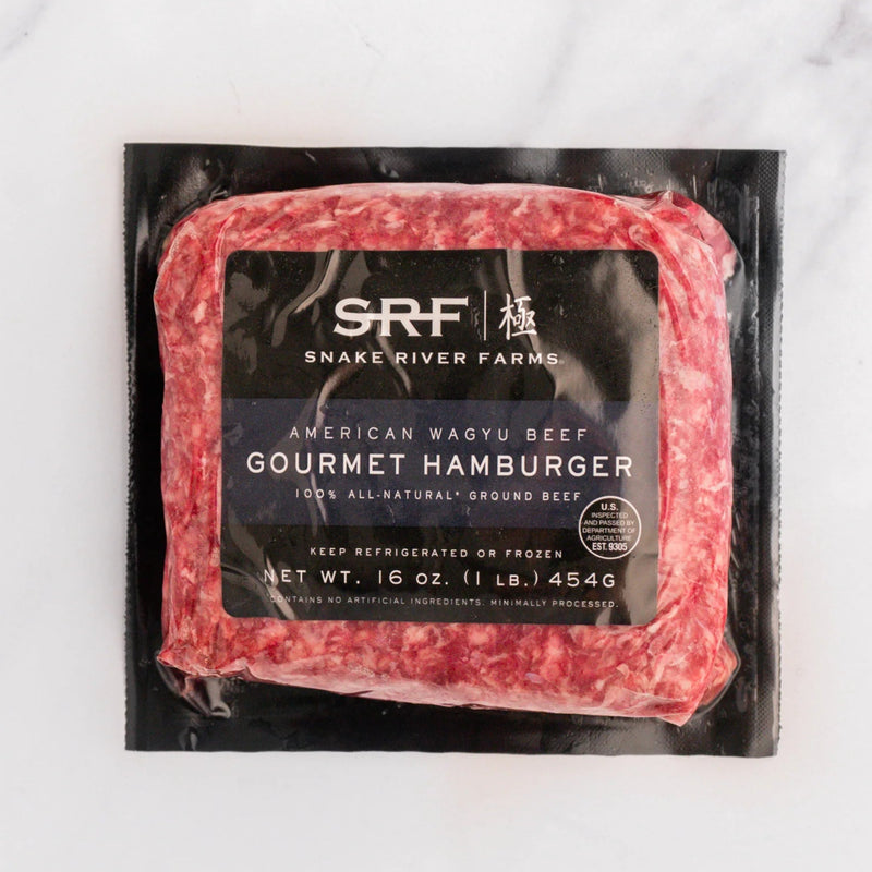 A 16 oz package of SRF Gourmet Hamburger American Wagyu Beef, featuring a marbled red and white ground beef product in a black plastic vacuum-sealed bag with a black label, set on a white marble surface.