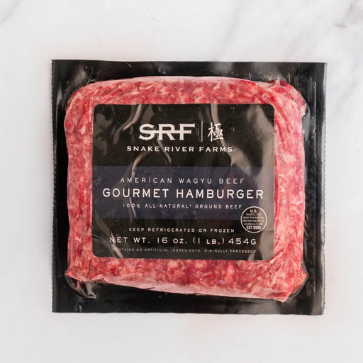 A 16 oz package of SRF Gourmet Hamburger American Wagyu Beef, featuring a marbled red and white ground beef product in a black plastic vacuum-sealed bag with a black label, set on a white marble surface.