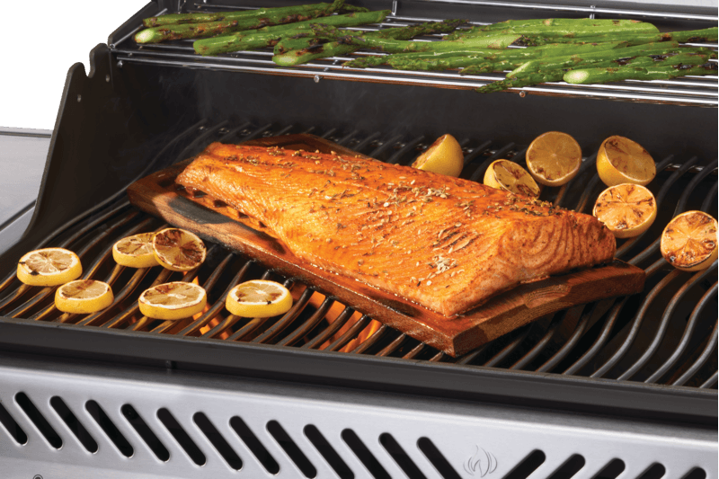 Grilled salmon and lemons on a Napoleon Rogue PRO 625 grill with asparagus in the background.