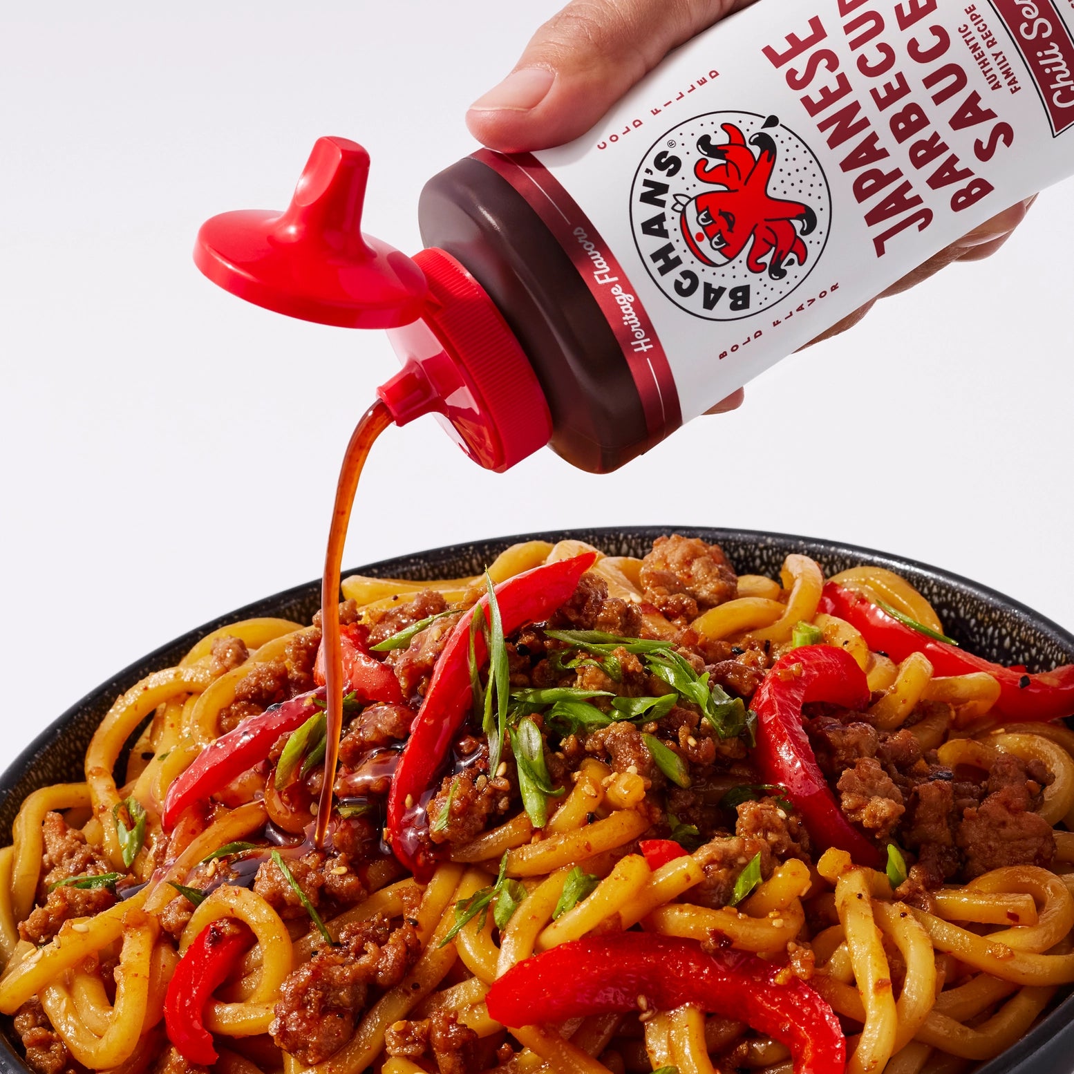 Bachan's chili sesame barbecue sauce being poured over Japanese noodle stir-fry with bell peppers.
