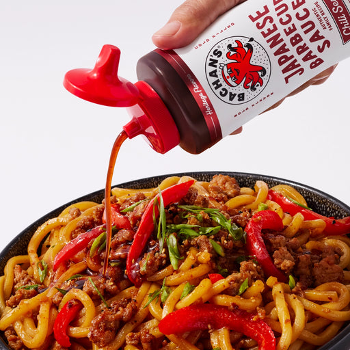 Bachan's chili sesame barbecue sauce being poured over Japanese noodle stir-fry with bell peppers.